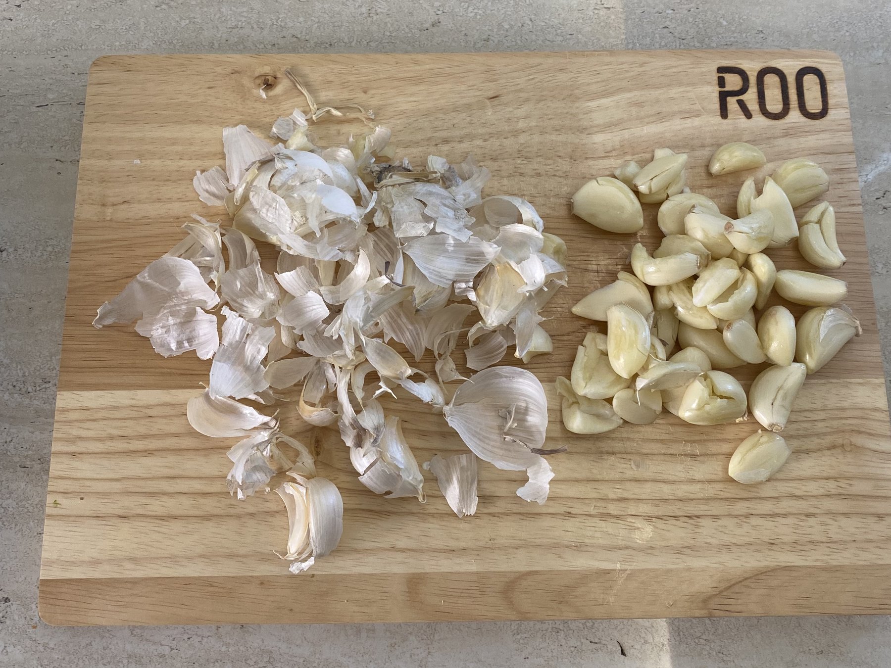 Garlic skins covering half of a cutting board, with the peeled cloves squeezed onto the other half